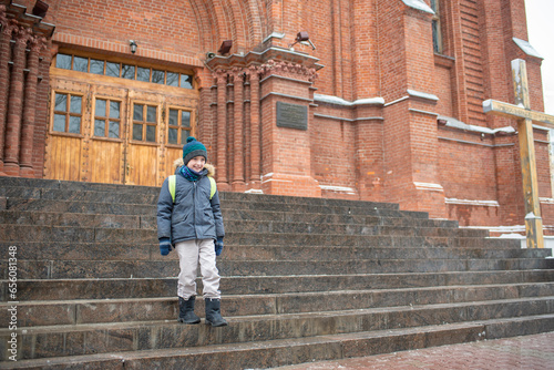 happy child goes to catholic church on sunday in winter. A 10-year-old boy stands in front of a Catholic cathedral, goes to Sunday Christian school.
