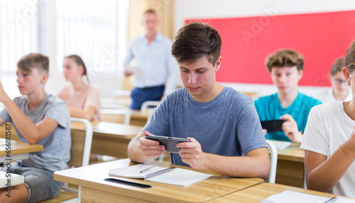 Concentrated high school student using smartphone to find necessary information on lecture in class. Concept of using mobile technology in education