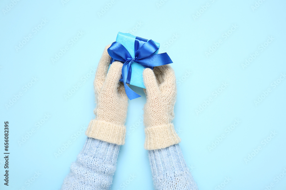 Female hands in warm mittens with Christmas gift on color background, closeup