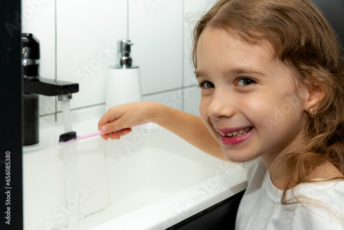 A happy little girl brushes her teeth in front of a mirror in the bathroom. Morning routine. Hygiene. High quality photo