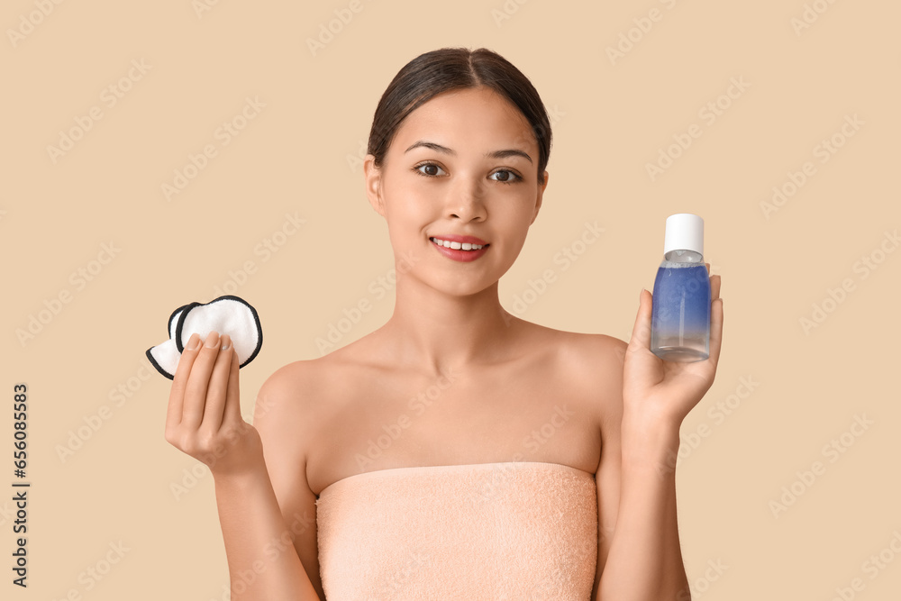 Young Asian woman with bottle of micellar water and reusable cotton pads on beige background Young Asian woman with bottle of micellar water and reusable cotton pads on beige background