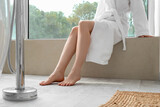 Barefoot woman sitting on windowsill in bathroom with floor heating