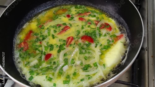Close up on handmade scrambled eggs with onion, tomato, scallion, parsley, nira, butter, sizzling cooking in a cast iron frying pan. photo