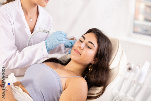 Young brunette girl having facial skin cleaning with beauty machine attachment