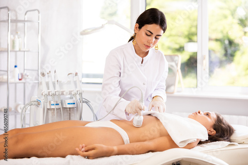 Female doctor making belly beauty procedure with ice hummer to female patient
