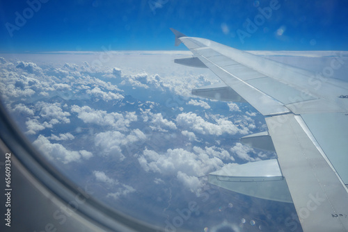 View from airplane window. Airplane wing against background of clouds in sky. View from passenger seat through window. Airplane flight. Background.
