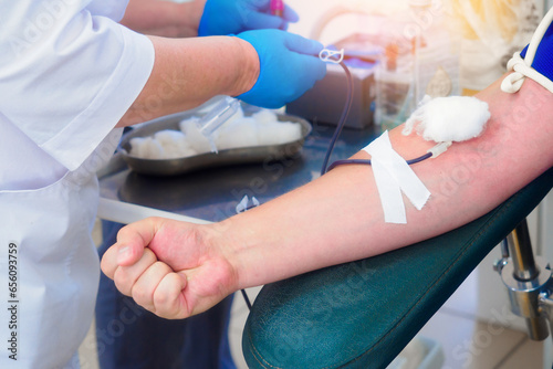 A donor donates blood at a blood transfusion station. Donor's hand close-up. Healthcare and charity. A medical worker wearing a gown and gloves inserts a needle into a vein. World Donation Day.