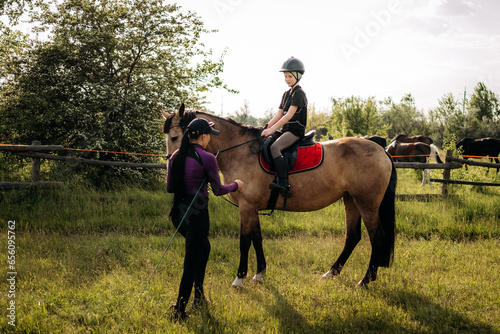 A teenage boy in a helmet learns horse riding in the summer, the instructor teaches the child equestrianism.