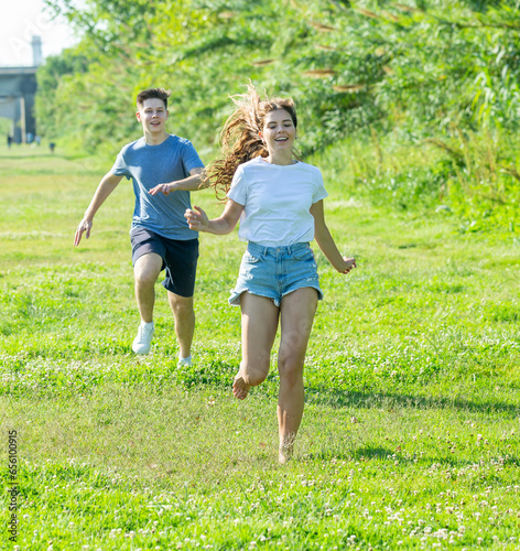 Fototapeta Naklejka Na Ścianę i Meble -  Two teenagers are running on the grass in summertime