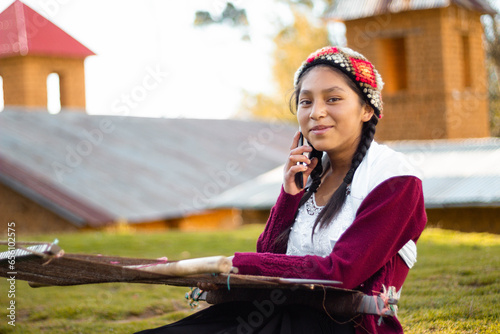 Foto de una feliz campesina caucásica hablando por teléfono inteligente y sosteniendo un tejido de manta artesanía peruana a mano en un atardecer en los Andes peruanos. Mujer usando teléfono móvil