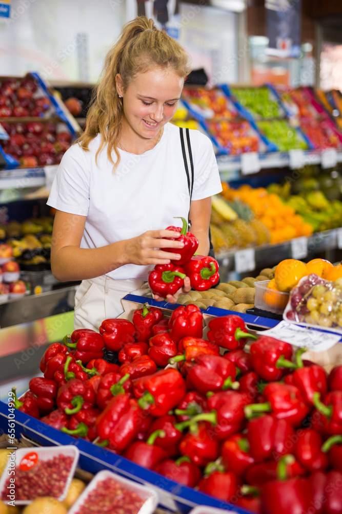 Portrait of teenage blonde girl customer buying red pepper at grocery shop