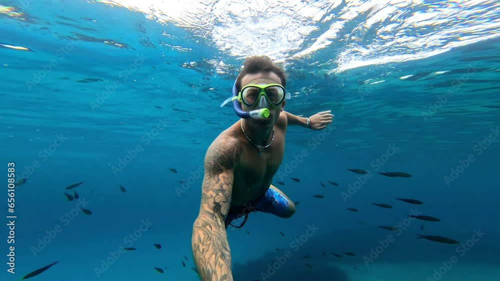 One young beautiful active man swimming and enjoying vacations outdoor in the sea snorkeling looking for fished and coral. Male person traveling holding camera having fun in the blue ocean
