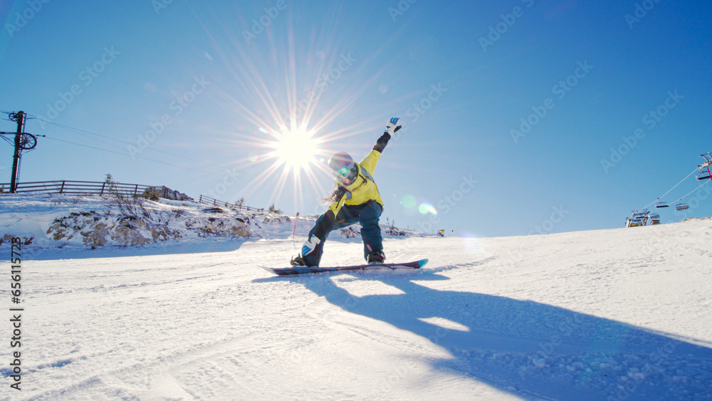 Girl snowboarding on slopes. Sun rays and flare visible.