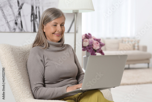 Beautiful senior woman using laptop in armchair at home © New Africa