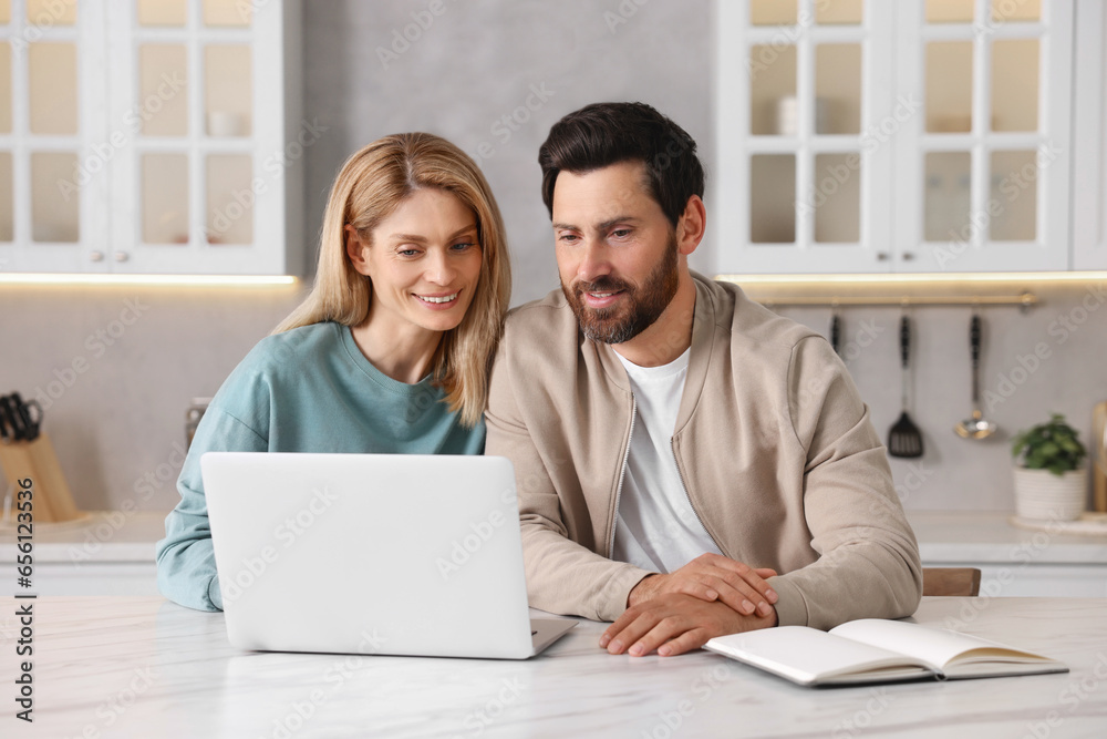 Happy couple with laptop at white table in kitchen Happy couple with laptop at white table in kitchen
