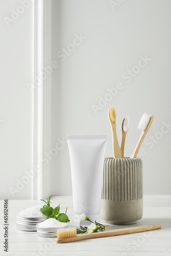 Toothbrushes, toothpaste and herbs on white wooden table
