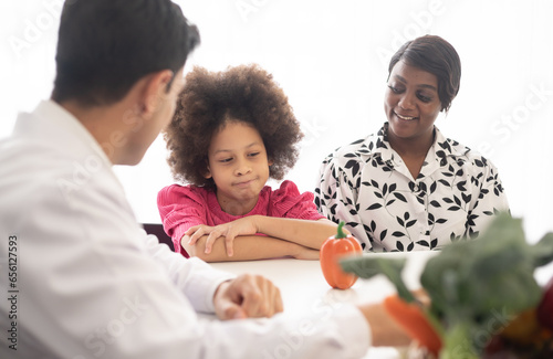 Hispanic nutritionist doctor consulting mixed-race child with her African American mother about a nutrition. Vegetables food - a new way for the good healthy and lifestyle.