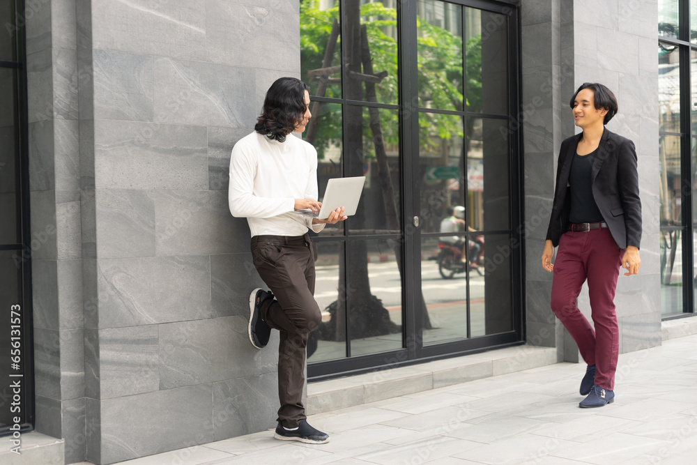 Businessman talking and working on a laptop against the modern building office. The colleague coworker discussion while standing.