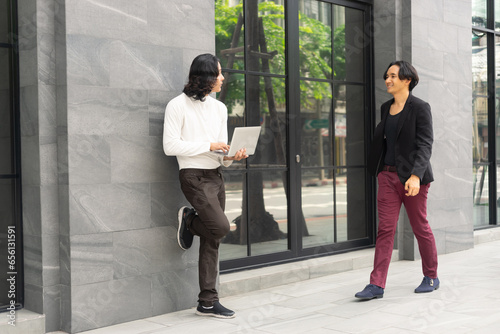 Businessman talking and working on a laptop against the modern building office. The colleague coworker discussion while standing.