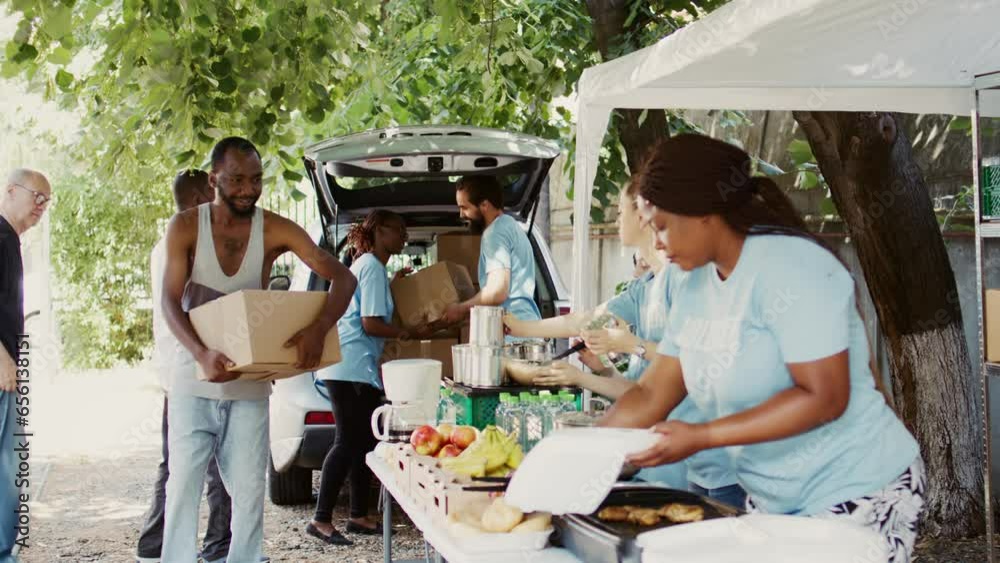 Diverse group distributing contribution boxes to those in need at a homeless and refugee shelter. Multiracial volunteers share essentials and provide support through a non-profit food bank. Handheld.