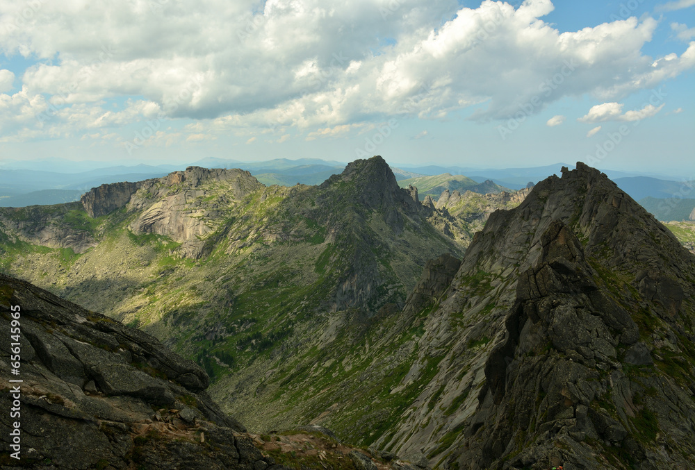 High rocky massifs with pointed peaks in the chain of a mountain range on a sunny summer day.