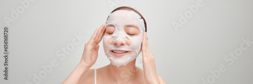 Beautiful asian woman applying paper sheet mask on her face white banner background