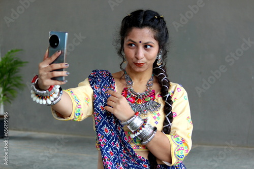 A woman taking her selfie after getting ready for navratri garba and dandiya. she is dressed up in traditional ghaghra choli, chaniya and patola dupatta with hand made oxidized ornaments jewellery.   photo
