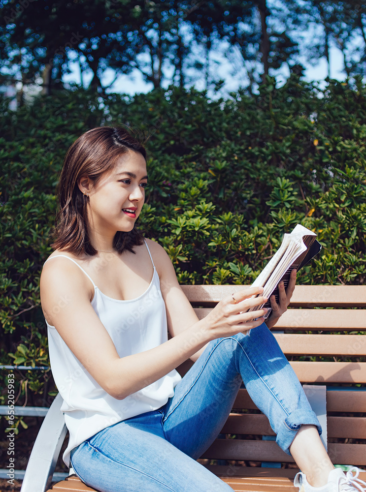 Naklejka premium Young Asian woman reading book on bench in park