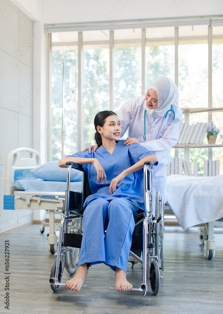 Asian professional successful experienced muslim female doctor in white lab coat with hijab stethoscope helping supporting assisting injury senior male patient on wheelchair in hospital ward.