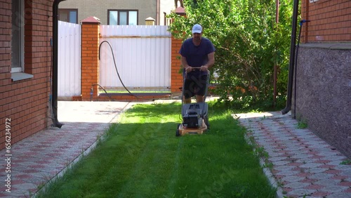 The man is working in the garden. Mowing grass with a lawn mower.