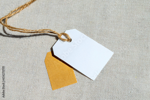 Two rectangular tags with a rope on a gray fabric. Blank label mockup with price tag