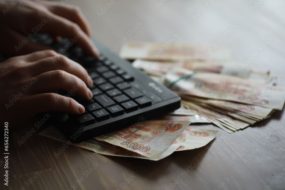 Stacks of 5000 ruble banknotes on the table next to the laptop. Savings and investments in the conditions of sanctions and inflation. Stacks of 5000 ruble banknotes on the table next to the laptop. Savings and investments in the conditions of sanctions and inflation.