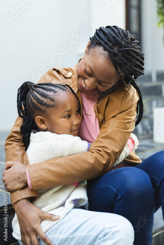 Happy african american mother and daughter embracing on steps in front of house