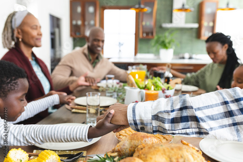 Happy african american multi generation family holding hands at thanksgiving dinner