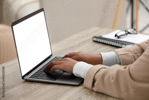Woman using laptop at wooden desk indoors  closeup