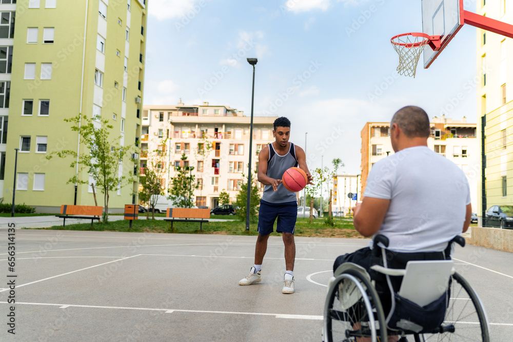 Obraz premium Mature man in the wheelchair coaching basketball to a young black man at the youth center before tryouts