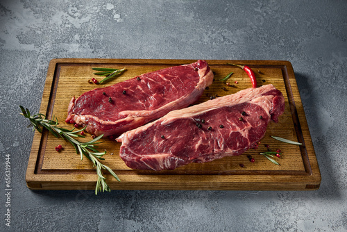 Side view highlighting raw striploin and New York steaks on a wooden board. The detailed texture of the beef is evident, all against a neutral gray setting