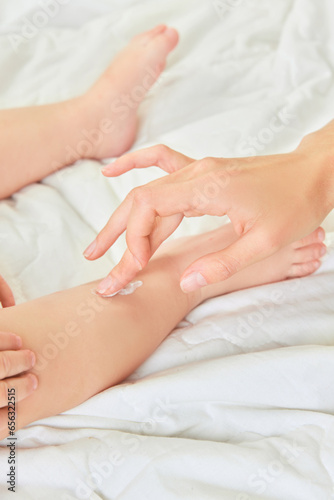 Female hand, mother applying moisturizing body cream on legs of her child, toddler. Home care. Concept of childhood, kids cosmetology and natural cosmetics, body care
