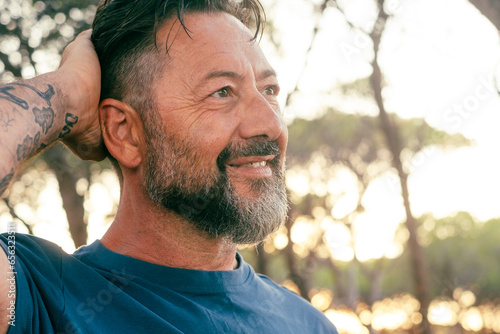 Close up face view portrait of adult man smiling and enjoying serene leisure activity in outdoor with trees and sunset light in background. Concept of happy lifestyle people. Handsome male mature photo