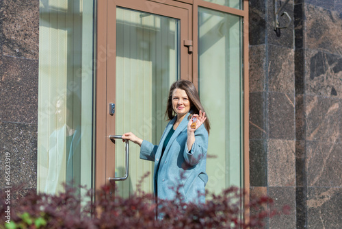 Happy woman realtor handing key keychain next to door of house. Female landlord smiling holding housekey. Buy sale rent real estate. mortgage, apartment renting, moving, relocation, property.  photo