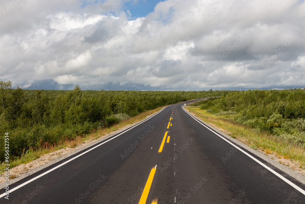 Newly paved road with endless yellow stripes between forests and blue sky with big clouds Newly paved road with endless yellow stripes between forests and blue sky with big clouds