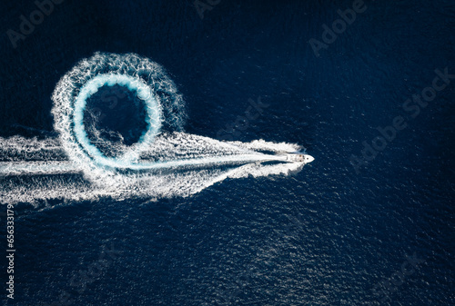 Aerial top view of a motor powerboat forming a circle of waves and bubbles with its engines over the blue sea photo