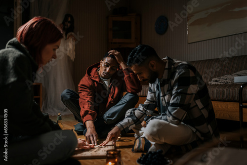 Friends touching ouija board while ghost in background at cabin photo