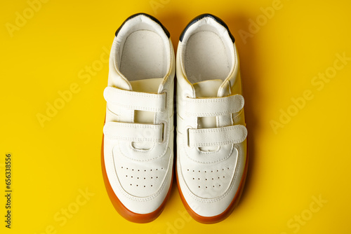 White leather sneakers with advehise fasteners on yellow background