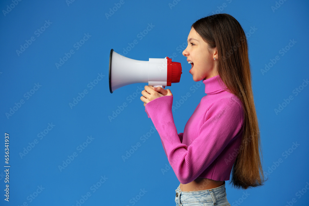 Teen girl making announcement with megaphone on blue background Teen girl making announcement with megaphone on blue background