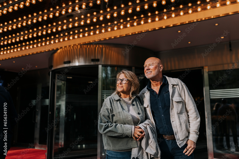 Smiling male and female senior friends standing outside movie theater