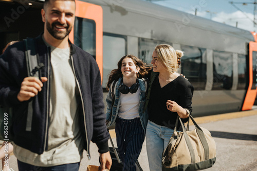 Happy family disembarking from train at station during sunny day