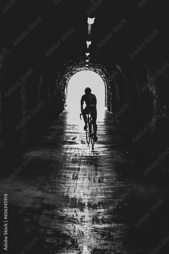 Cyclist on the road bike in the narrow tunnel. Silhouette of athlete. Black and white photography.