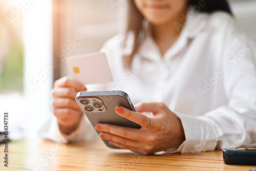 Happy young woman holding credit card and using smart phone, shopping on Internet or payment online