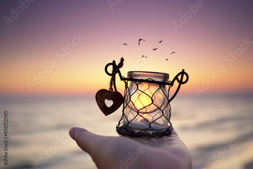 Obraz na plátne schöne Laterne mit Herz am Strand im Sonnenaufgang in der Hand halten